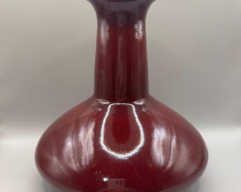 May include: A deep red ceramic vase with a wide base and a narrow neck. The vase has a glossy finish.