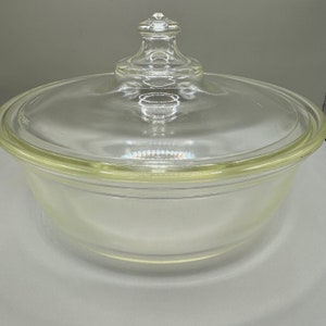 May include: A clear glass baking dish with a lid. The dish is round and has a slightly flared rim. The lid has a knob on top.