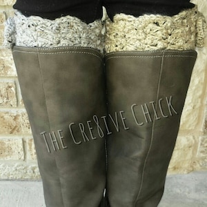May include: A pair of brown leather boots with a crocheted cuff in beige and gray. The boots have a buckle detail and the text "THE CREATIVE CHICK" is visible on the boots.