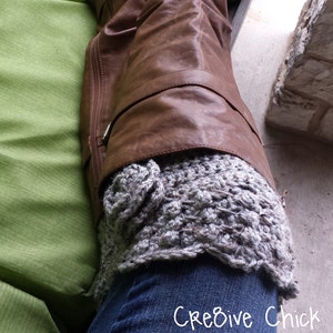 Puede incluir: Botas de cuero marrón con un calienta piernas de ganchillo gris. Las botas tienen un detalle de hebilla y el calienta piernas tiene un patrón texturizado.