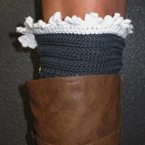 Puede incluir: Calentadores de piernas de crochet gris con un borde de encaje blanco tejido a crochet. Los calentadores de piernas se llevan sobre botas marrones.