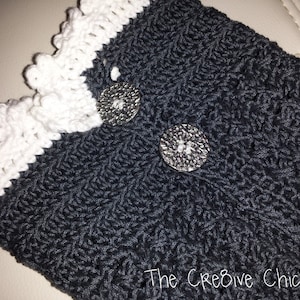 Pode incluir: Aquecedores de pulso de crochê preto com uma borda de crochê branca e dois botões prateados.