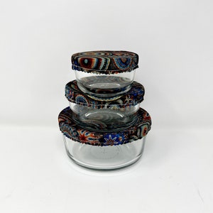 May include: Three glass bowls with reusable fabric covers. The covers are patterned with colorful circles and swirls in shades of blue, red, and brown.