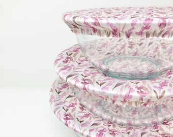 May include: Three glass bowls with floral patterned fabric covers. The covers are white with a pink and brown floral design.