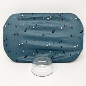 May include: A blue fitted crib sheet with a white and black mountain and forest print. The sheet is on a white surface with a clear glass bowl.