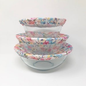 May include: Three glass bowls with floral patterned fabric covers. The covers are in shades of pink, blue, and yellow.