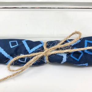 以下が含まれることがあります： 青と白のパターンが施された布が、ナチュラルな麻ひもで結ばれています。布は折り畳んで中央で結ばれています。
