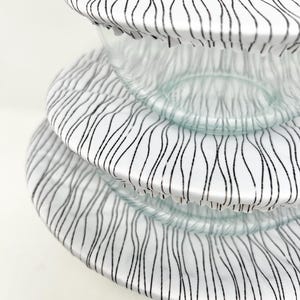 May include: Three white reusable silicone bowl covers with a black wavy line pattern. The covers are stacked on top of each other.