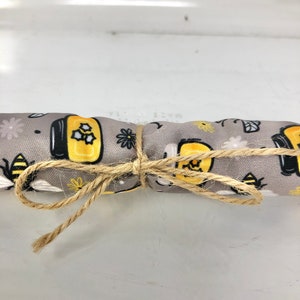 以下が含まれることがあります： 蜂とハニカムのパターンが描かれたグレーの生地が、紐で結ばれて巻かれている。