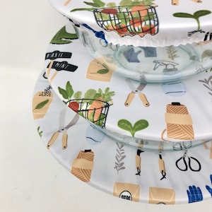 May include: Three glass bowls with white fabric covers. The covers feature a light blue background with gardening-themed illustrations, including scissors, baskets of produce, and the text "Basil Mint".