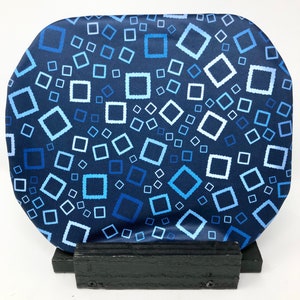 May include: A blue and white patterned fabric cushion with a geometric design of squares. The cushion is displayed on a black wooden stand.