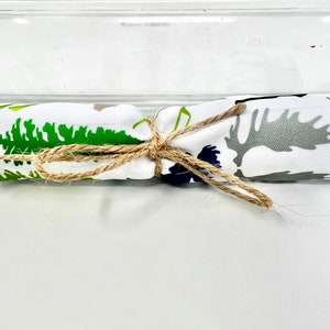 May include: A white fabric with a green tree and gray moose design is tied with a brown twine bow.