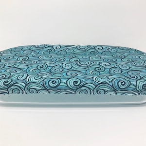 以下が含まれることがあります： 長方形のベーキングディッシュ用の青と白のパターンのファブリックカバー。カバーは渦巻く波のデザインです。