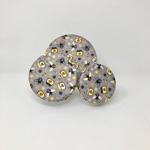 May include: Three round gray fabric lids with a repeating pattern of black bees and yellow honey jars on a white background.