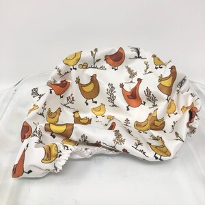 May include: White fabric shower curtain with a repeating pattern of brown and yellow chickens and eggs. The curtain is gathered and bunched up, showing the pattern.