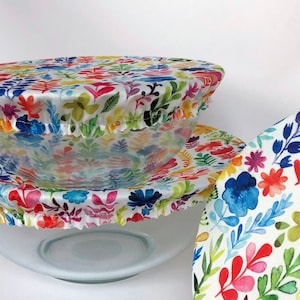 May include: Two reusable food covers with a colorful floral pattern. The covers are made of a fabric that is both washable and reusable. The covers are a great way to keep food fresh and prevent spills.