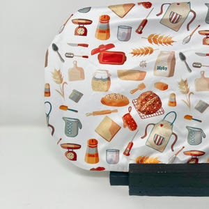 May include: White fabric patterned with baking-themed illustrations. The design includes aprons, measuring cups, scales, bread, and the word "Flour". The color scheme features red, orange, and brown accents.