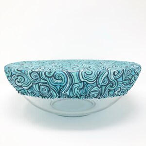 May include: A blue and black patterned fabric bowl cover. The cover is made of a soft, stretchy fabric and is designed to fit over a variety of bowl sizes.