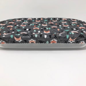 Könnte beinhalten: Ein grauer Stoff-Geschirrtuch mit einem geometrischen Muster mit Füchsen, Dreiecken und Bäumen. Das Tuch liegt auf einer durchsichtigen Glas-Backform.