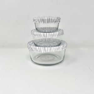 May include: Three glass storage containers with black and white striped lids. The lids are made of a flexible material and can be used to cover a variety of sizes of containers.