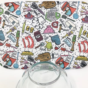 以下が含まれることがあります： キッチンをテーマにした白い楕円形の布地で、カラフルなキッチン用品、食べ物、テキストのパターンが描かれています。テキストには、「mouth watering」、「delicious」、「mmm」、「so good」、「spicy」、「yum」が含まれています。