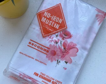 May include: A package of two standard size pillow cases. The pillowcases are white with a pink floral pattern. The package has a red and orange label that reads "NO-IRON MUSLIN". The package also reads "SECONDS" and "50% Polyester 50% Cotton".