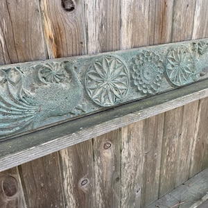 May include: A weathered wooden panel with carved floral designs. The panel is painted a light green color and has a rustic appearance.