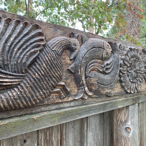May include: A carved wooden panel with a detailed design of a bird, fish, and floral motifs. The panel is dark brown and has a weathered look.