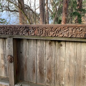May include: A close-up of a wooden fence with a carved wooden panel at the top. The panel features intricate designs of leaves and flowers.