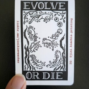 May include: A white sticker with a black illustration of tadpoles and frogs, with the words "EVOLVE OR DIE" in bold letters. The sticker also includes social media handles and a link.