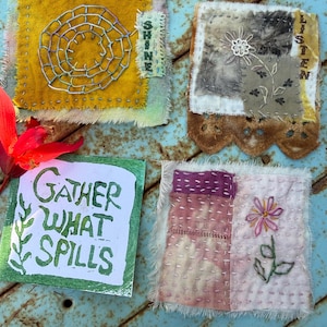 May include: Four handmade fabric art pieces. One yellow square features a stitched spiral and the word "SHINE". Another has a floral design and the word "LISTEN". A third says "GATHER WHAT SPILLS". The last has a flower.