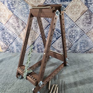 May include: A dark brown wooden adjustable frame with a triangular structure, featuring multiple pre-drilled holes along the side rails, metal wing nuts at the joints, a horizontal top bar with a spring, and a patterned fabric strap attached.