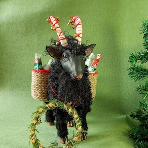 Puede incluir: Una caprichosa figura de cabra negra con cuernos de bastón de caramelo y una corona. La cabra lleva cestas llenas de regalos envueltos. Los cuernos de la cabra están adornados con campanas. La figura está sobre un fondo verde.