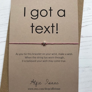 May include: A greeting card with the text "I got a text!" in black font. A pink string bracelet with a star charm is attached. The card includes a wish-making message and the Etsy shop name.