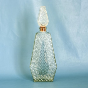 Peut inclure: Une carafe en verre transparent avec un motif en forme de diamant et un bouchon en liège. La carafe est sur un fond bleu clair.