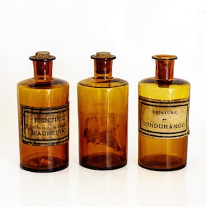 Juego de 3 frascos de farmacia con etiquetas, de vidrio antiguo color ámbar oscuro y marrón.