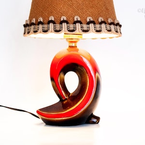 Peut inclure: Lampe de table vintage avec un abat-jour en toile de jute marron et une garniture décorative. Le pied a une forme abstraite unique avec une finition rouge, orange et marron brillante. La lampe a un cordon d'alimentation noir.