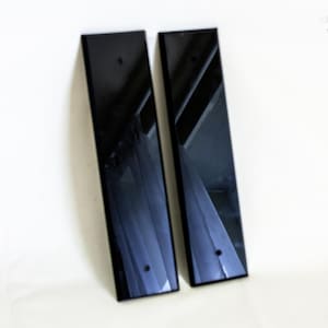 Può includere: Due pannelli rettangolari neri con finitura lucida sono esposti su sfondo bianco. Ogni pannello ha una piccola rientranza circolare vicino al fondo. I pannelli sono leggermente angolati, riflettendo la luce.