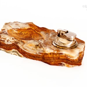 May include: A vintage ashtray and lighter set. The ashtray is carved from a layered, multi-toned stone with shades of brown, beige, and white. A silver-toned lighter sits on the ashtray. The set is on a white background.
