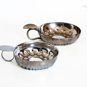 May include: Two circular silver-toned metal tart molds with fluted sides and a central hole. Each mold features a small, flat handle extending from the rim. The interior surfaces have a scalloped pattern, and the exterior edges show a twisted rope design.