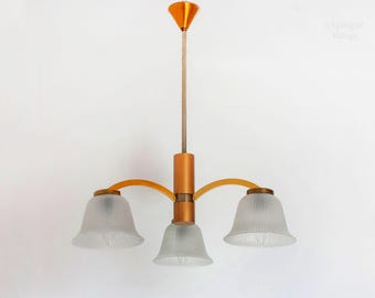 May include: A gold-toned chandelier with three white frosted glass shades. The chandelier has a curved arm design and a simple, elegant style.