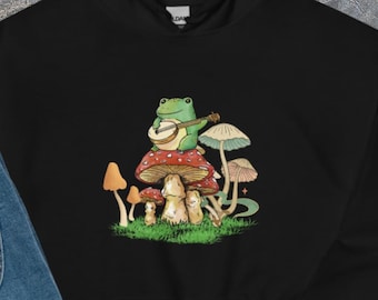 Felpa con cappuccio a forma di rana che suona uno strumento musicale, con design botanico a tema funghi in stile cottagecore.