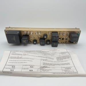 May include: A gold-toned electronic circuit board module featuring several black rectangular components, metallic circular connectors, and small silver pins. Below the module lies a white paper document titled Authorized Release Certificate.