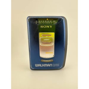 May include: A dark blue Sony Walkman WM-FX171 FM/AM radio cassette player. The device features a top-mounted frequency display, a central silver Mega Bass button, and an anti-rolling indicator. The front panel displays the Sony and Walkman logos.