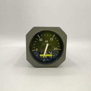 May include: A gray aviation fuel flow gauge with a circular black dial face. The gauge features white numerical markings from 5 to 20, the text FF and PPH X 1000, a white needle pointing near 5, and a horizontal digital display window with a yellow line.