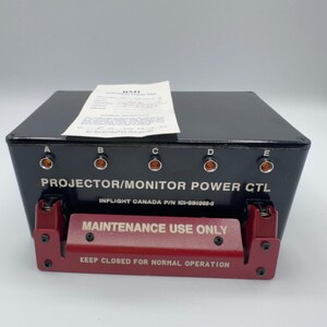 May include: A black rectangular projector/monitor power control unit with five ports labeled A through E. It features a red metal guard plate with the text MAINTENANCE USE ONLY and KEEP CLOSED FOR NORMAL OPERATION. A white paper document sits on top.