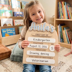 May include: An arched wooden sign with light blue 3D lettering reading Anila's. The sign features white horizontal panels with black text: First Day of Kindergarten, Today's Date August 12, 2026, Age 5, Things I Love: Drawing, dancing, and When I Grow Up, I Want to Be a Veterinarian.