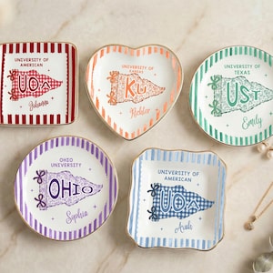 Puede incluir: Una colección de platos decorativos de cerámica en varias formas, cada uno con un diseño de banderín universitario. Los platos están adornados con nombres y nombres de universidades, incluyendo "University of American", "University of Kansas", "University of Texas" y "Ohio University".