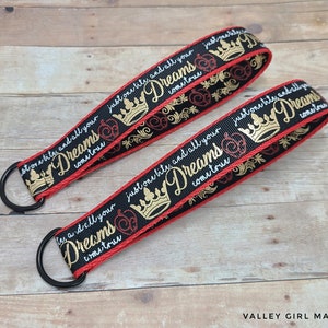 May include: Two black key fobs with red trim and gold text that reads "just one bite and all your dreams come true." The key fobs have a gold crown and apple design. Each fob has a black metal ring.