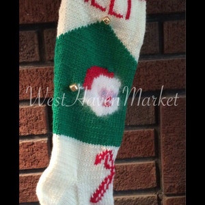 May include: A white, green, and red knitted Christmas stocking with the name "ALLI" embroidered on the front. The stocking has a Santa Claus face and a candy cane design.